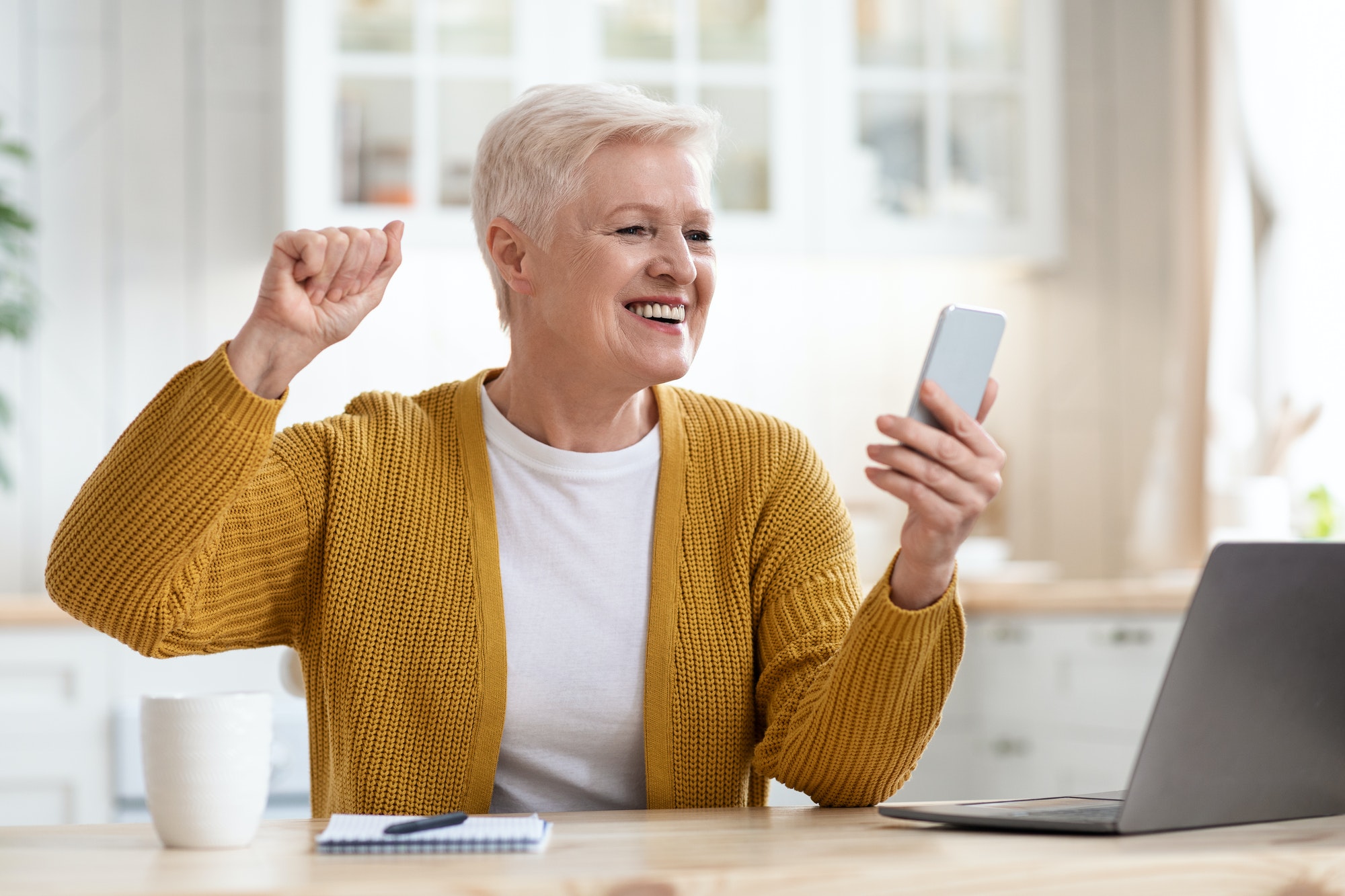 Excited grandmother holding smartphone and raising fist up